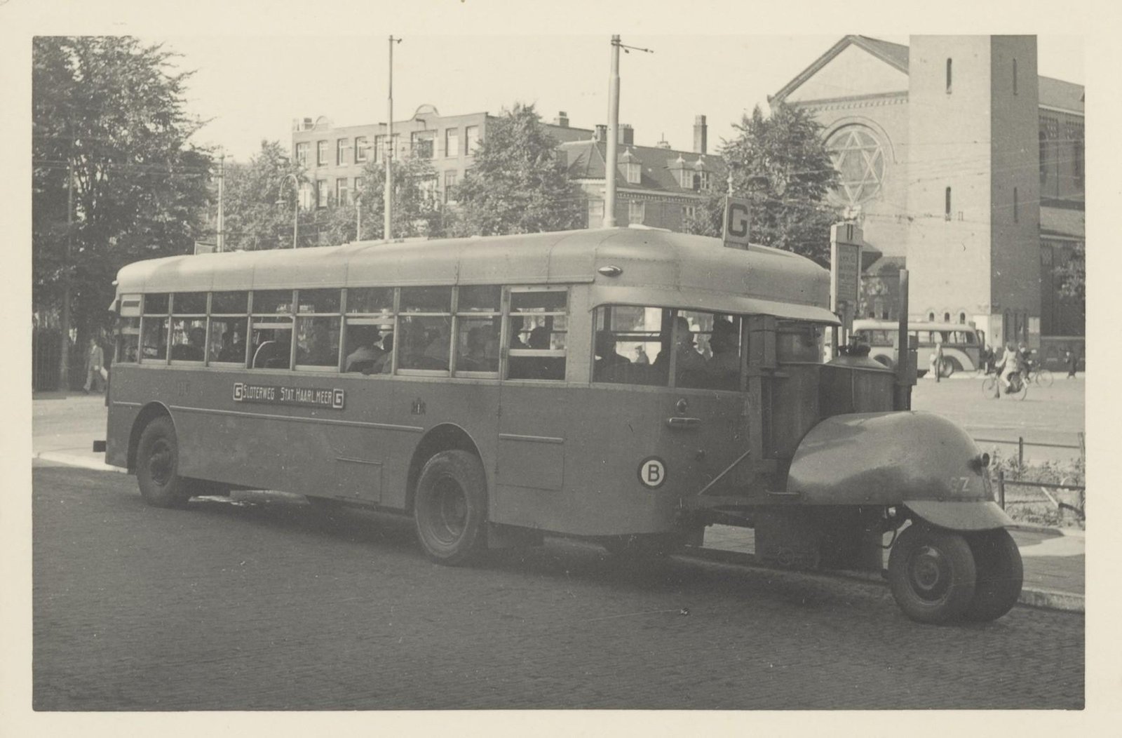 Autobus van lijn G met houtgasgenerator op de Amstelveenseweg bij het Haarlemmermeerstation, met op de achtergrond de Sint-Agneskerk (1943)