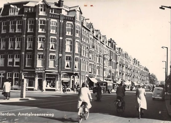 Straatbeeld van de Amstelveenseweg in Amsterdam met op de hoek stoffenwinkel Van Dijk Stoffen, op een ansichtkaart uit de jaren vijftig.