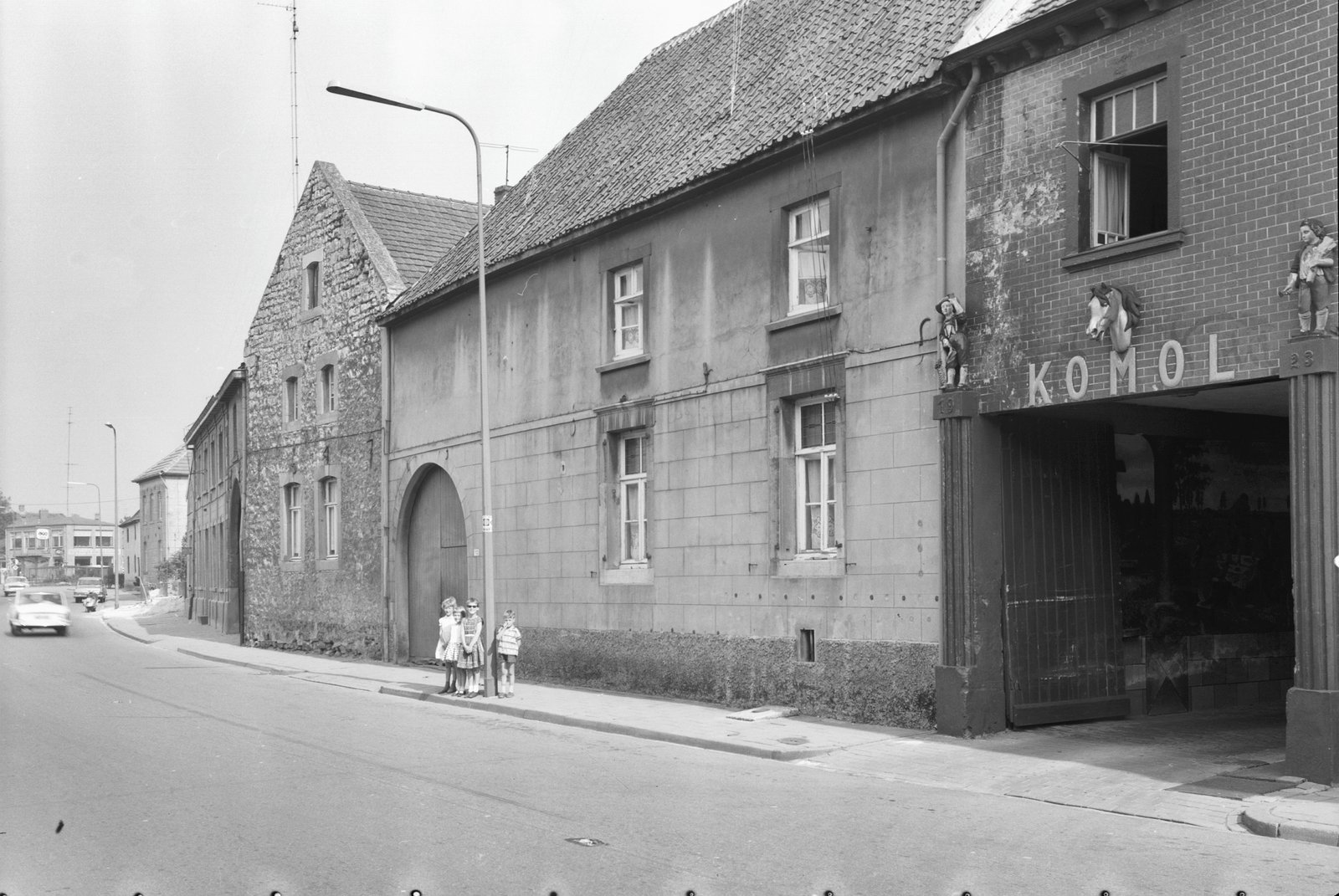 Straatbeeld van de Heerlerweg 108-110 in Kunrade met de poort van limonadefabriek KOMOL en poserende kinderen op de voorgrond (1963)